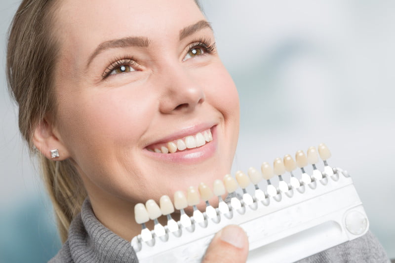 Woman comparing teeth with tooth shade guide - Cosmetic Dentistry in St. George, UT