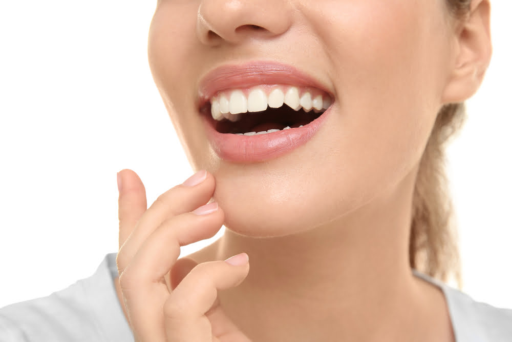 A close-up of a woman smiling, showing straight, white teeth and healthy gums, as she touches her chin - Dentist St George Utah A close-up of a woman smiling, showing straight, white teeth and healthy gums, as she touches her chin - Dentist St George Utah