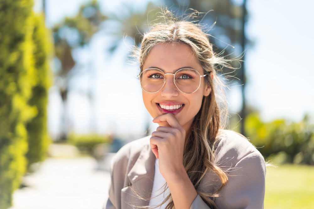 A woman wearing glasses smiles brightly outdoors, showcasing her white teeth and healthy dental care - Dentist St George Utah A woman wearing glasses smiles brightly outdoors, showcasing her white teeth and healthy dental care - Dentist St George Utah