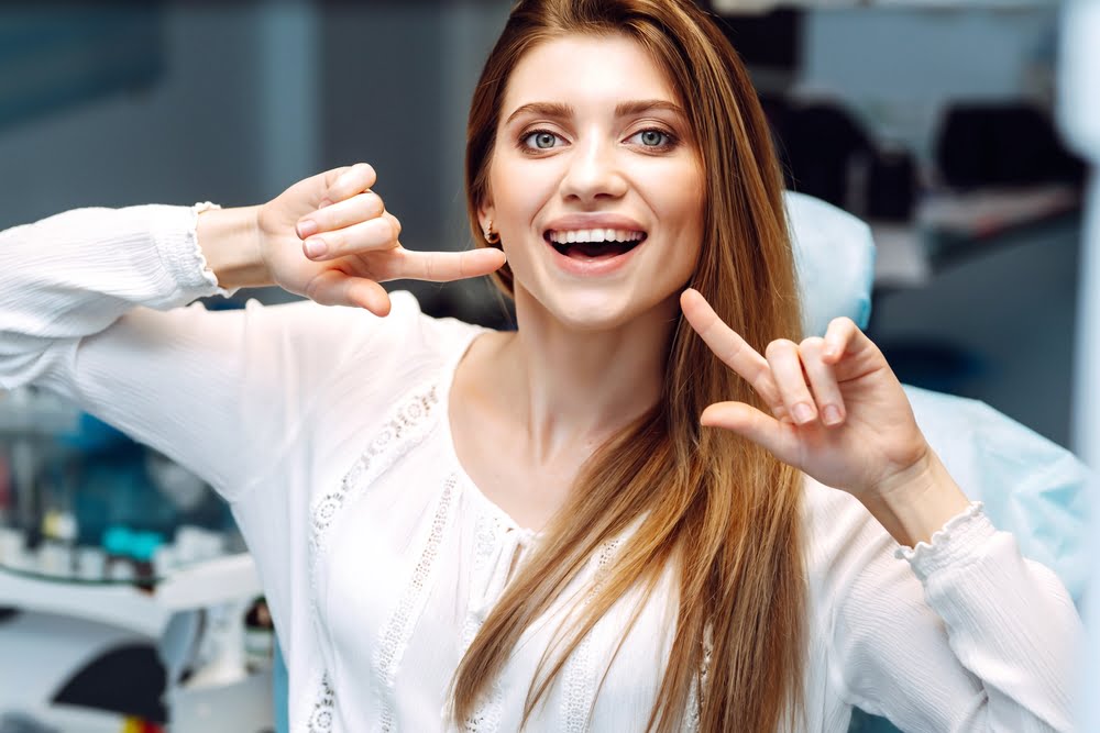 A woman in a dental clinic smiles and points to her teeth, showing off her healthy smile after a dental treatment - Dentist St George Utah A woman in a dental clinic smiles and points to her teeth, showing off her healthy smile after a dental treatment - Dentist St George Utah