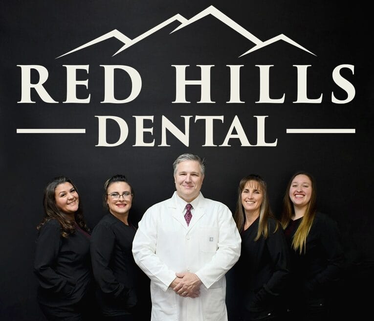 A woman with a bright smile, showing straight white teeth, rests her head on her hand, showcasing healthy dental care - Dentist St George Utah